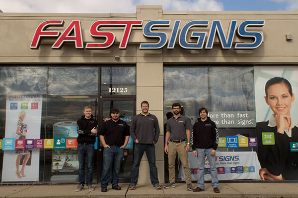 A FASTSIGNS team stands outside of their store front